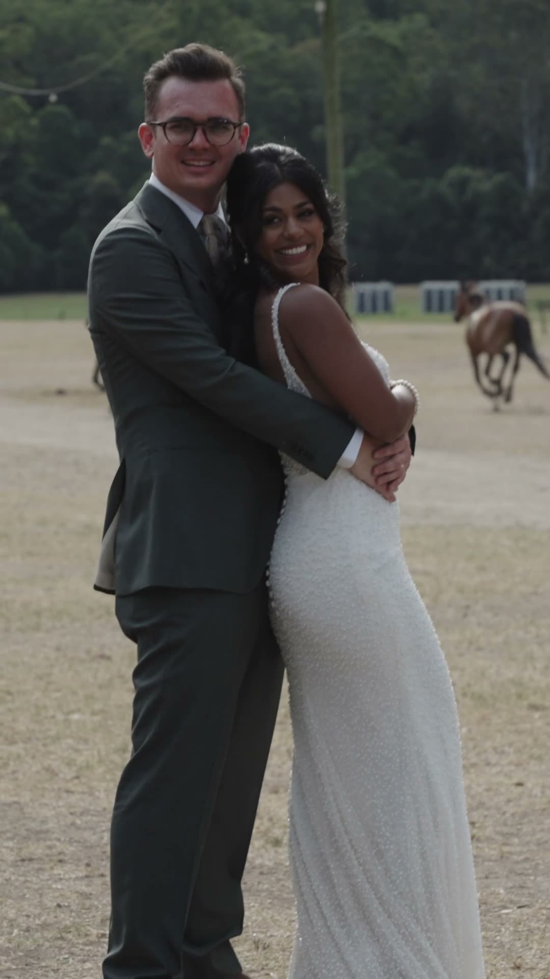 Riya & Matthias. Thirty-eight seconds, shot portrait. Opens on the couple's names set over gum-tree branches, then a kiss in close-up, their wedding sign, the two of them laughing in a paddock with horses running behind them, a black-and-white reception moment, and the bride's veil trailing in the wind through the trees.