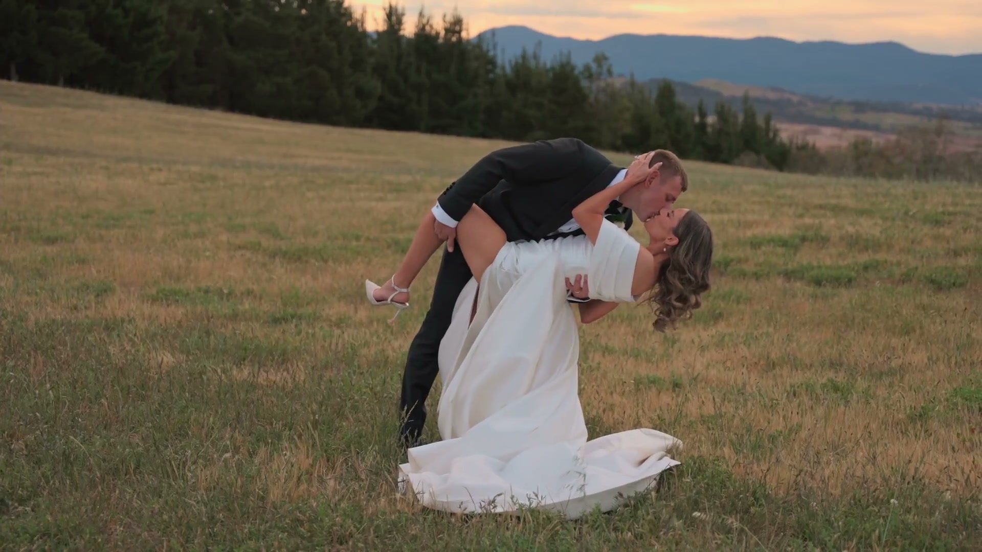 A groom dipping his bride in a dry golden paddock, hills behind them